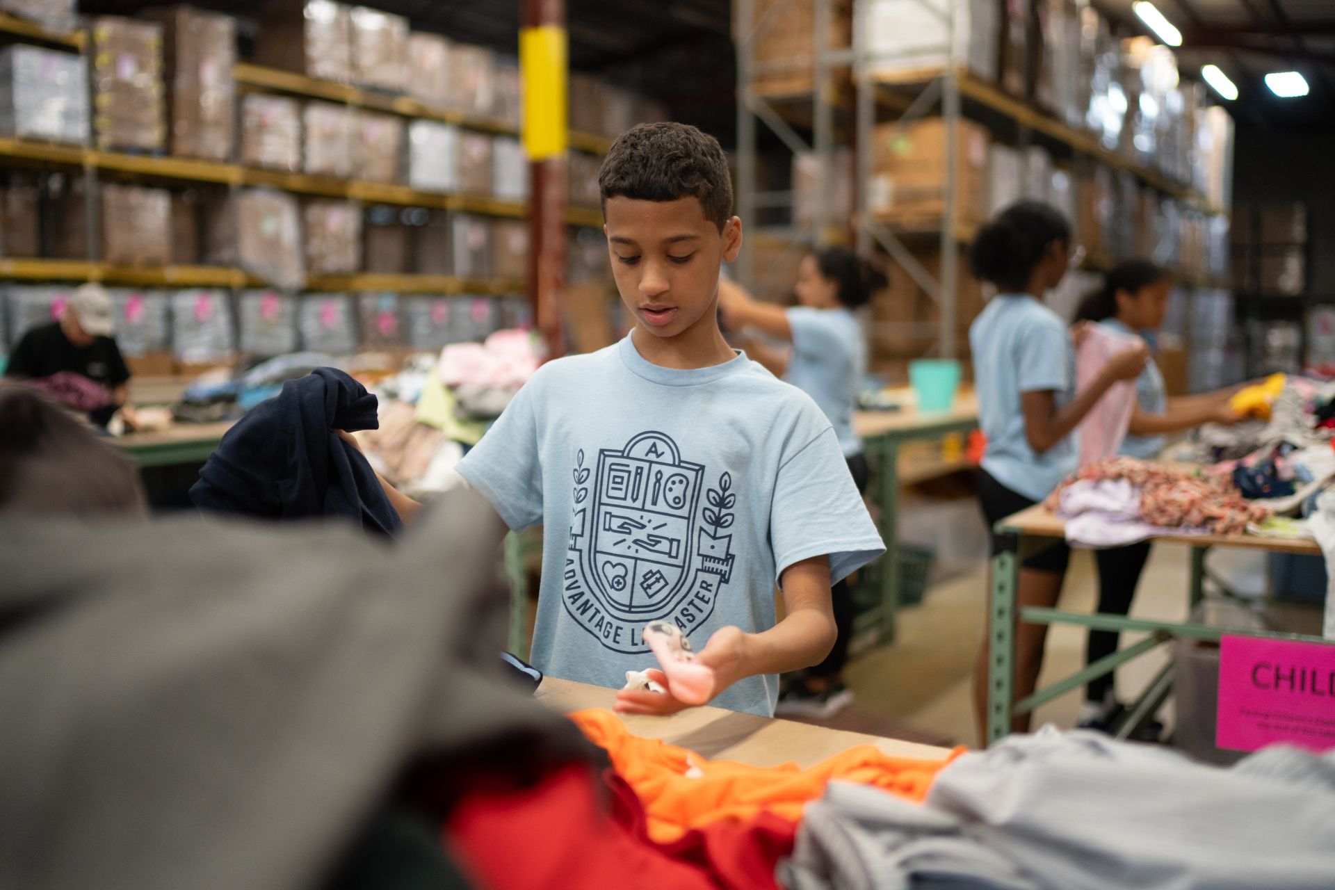 A young boy is working in a warehouse sorting clothes.