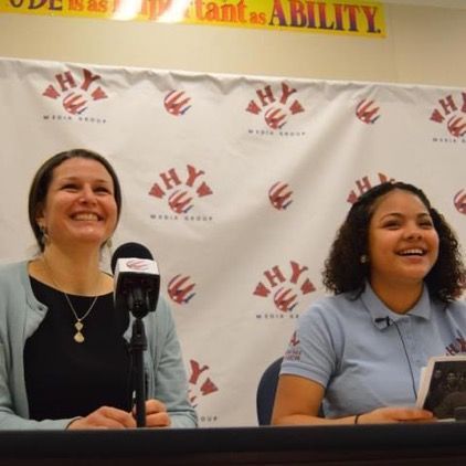 Two women are sitting in front of a banner that says