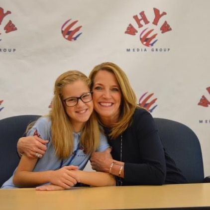 Two women are posing for a picture in front of a wall that says media group