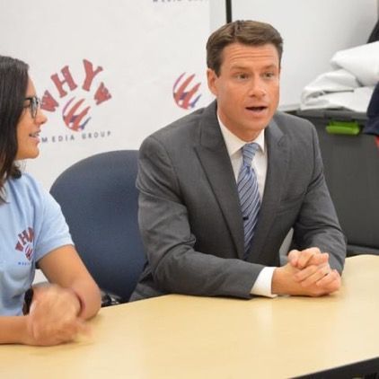 A man and a woman are sitting at a table in front of a sign that says hy