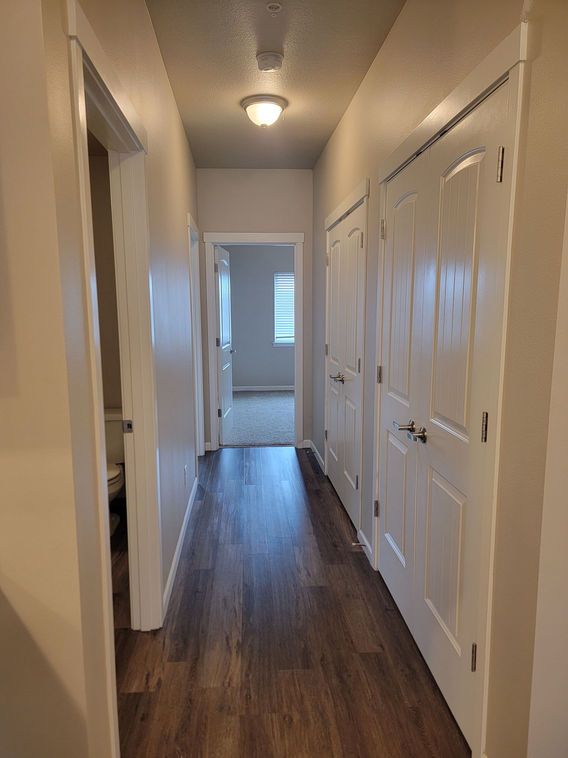 A long hallway with hardwood floors and white doors leading to a bedroom.