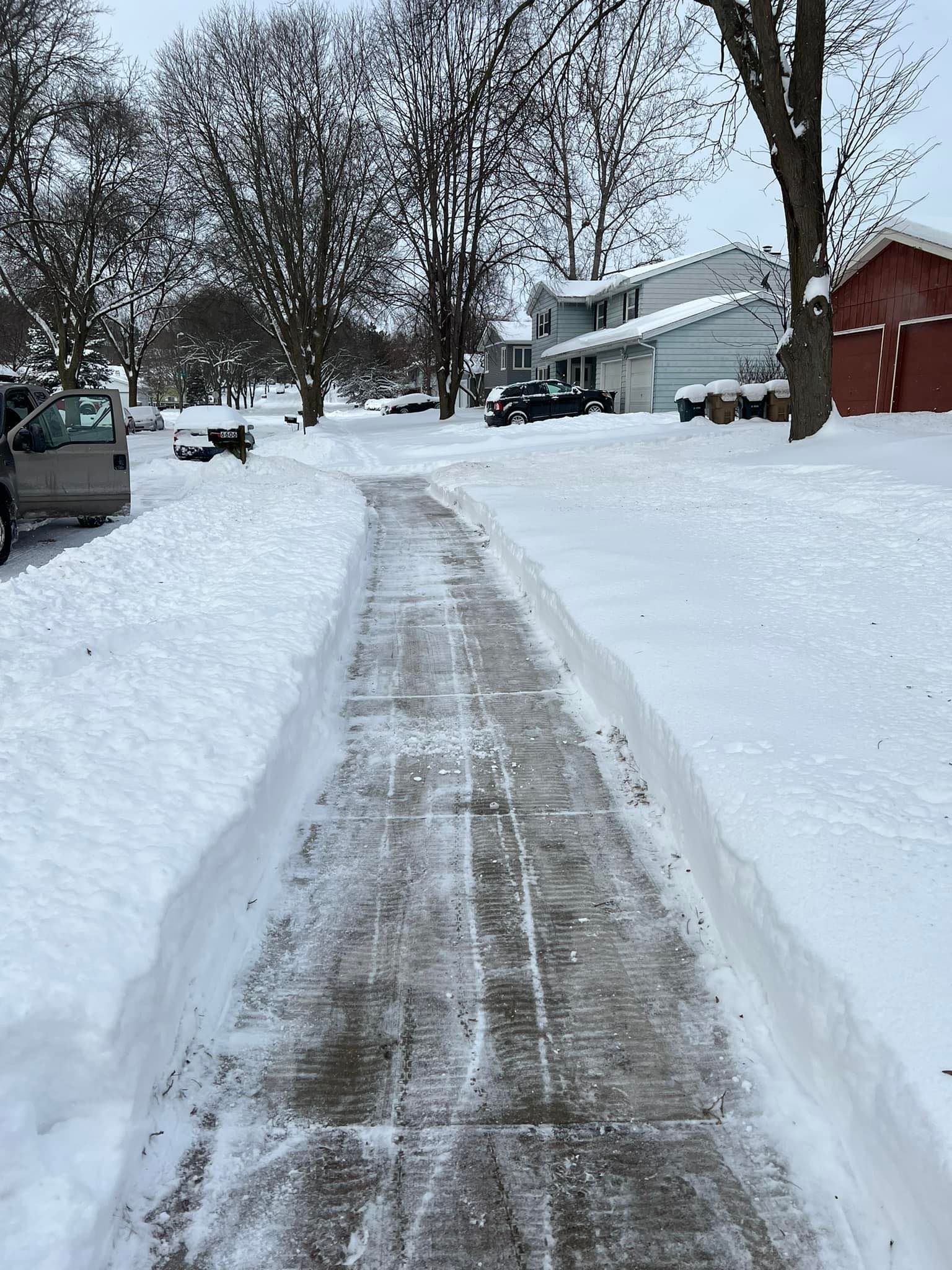 A snowy driveway with a car parked on the side of it.
