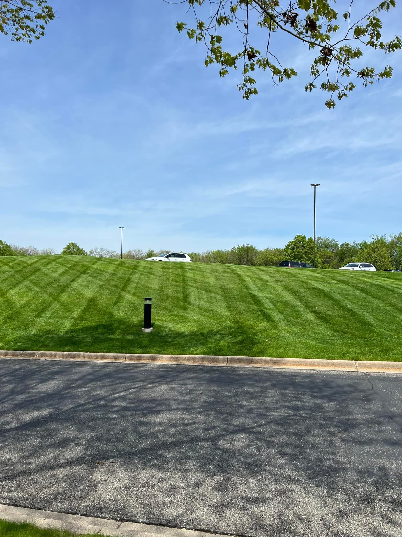 A lush green field with a parking lot in the foreground and a blue sky in the background.
