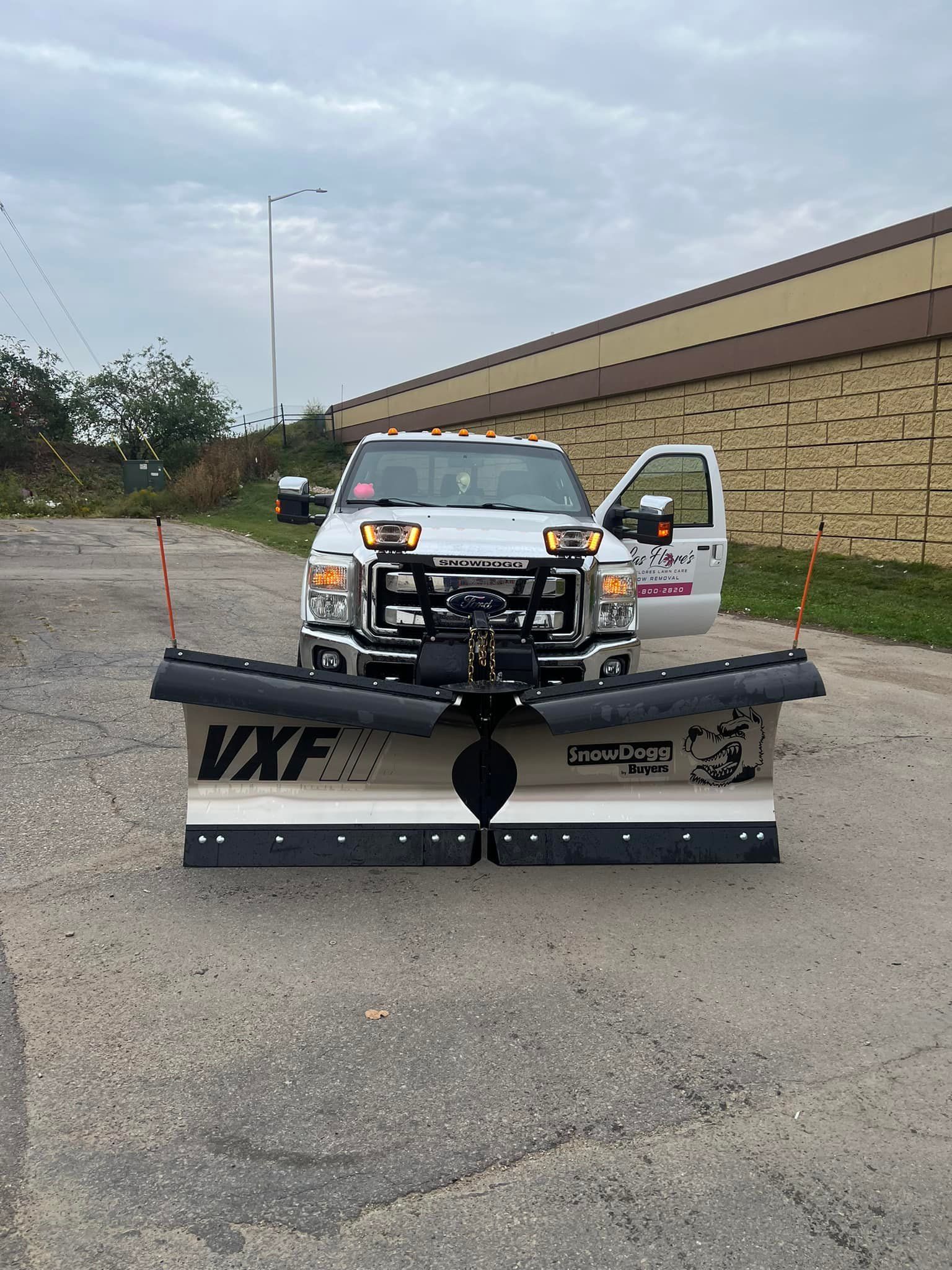 A white truck with a snow plow on the front is parked on the side of the road.