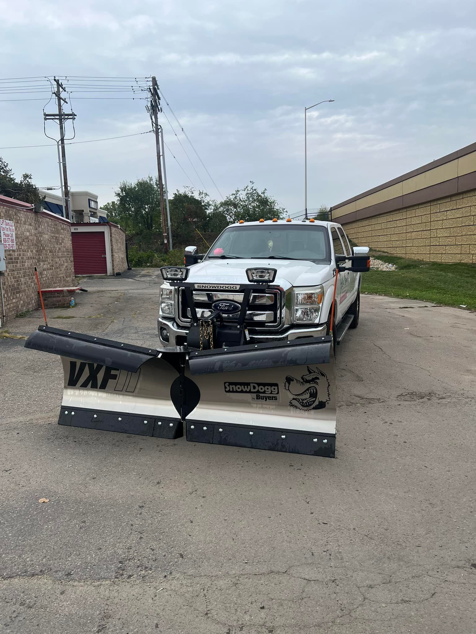 A white truck with a snow plow on the front is parked in a parking lot.