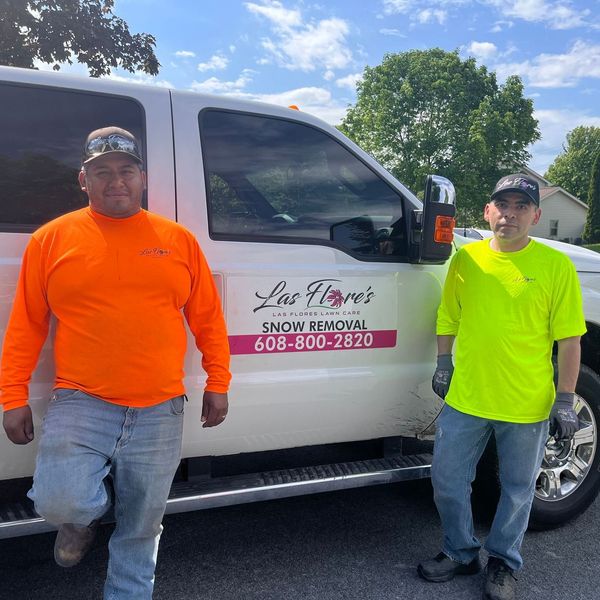 Two men are standing in front of a snow removal truck.