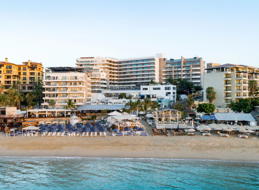Beachfront resort buildings behind rows of lounge chairs and umbrellas along the shore