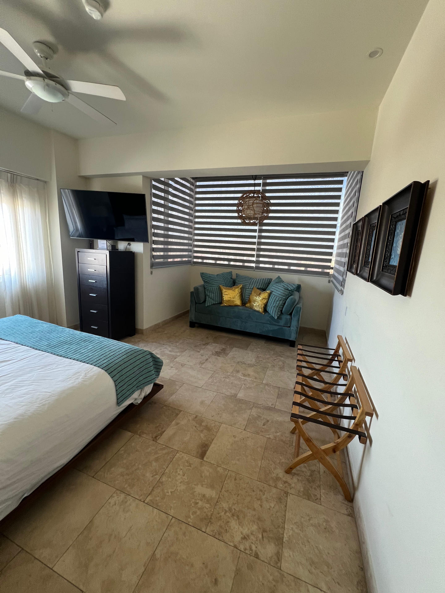 A bedroom with a bed , couch , television and a ceiling fan.
