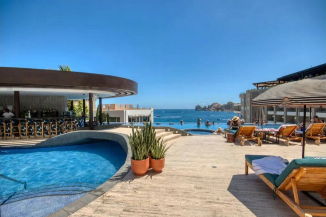 A large swimming pool surrounded by chairs and umbrellas next to the ocean.