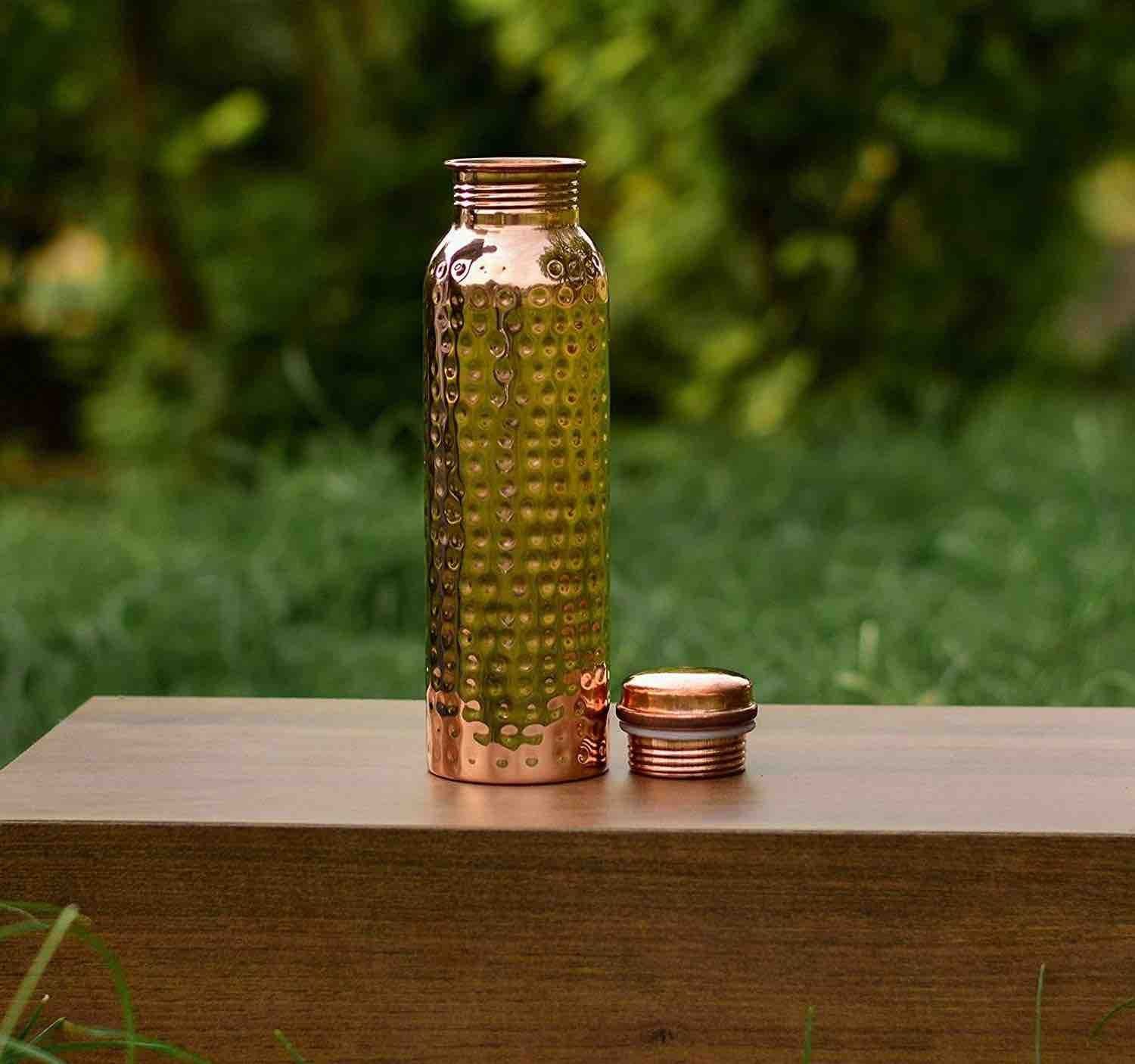 Picture of a copper water bottle sitting on a wooden table in a back yard