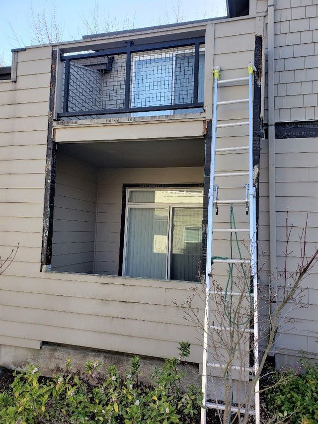 A ladder is sitting on the side of a building next to a balcony.
