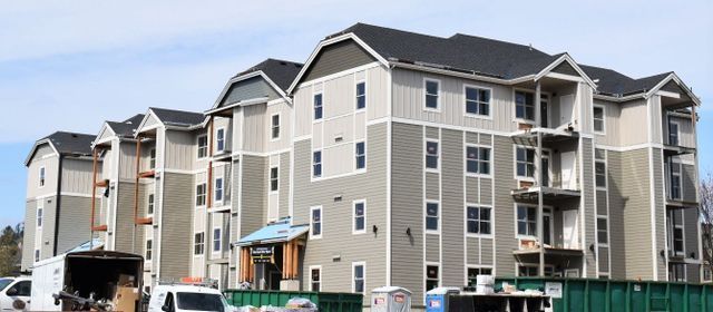A large apartment building under construction with a green dumpster in front of it.