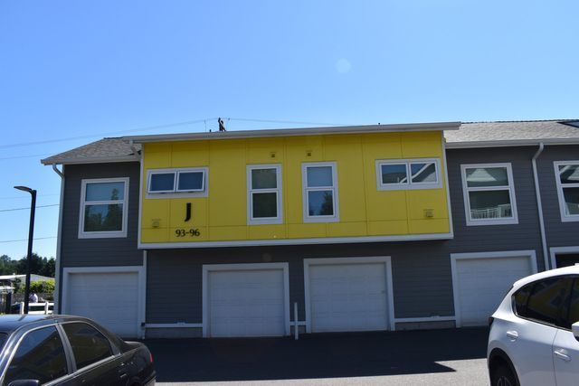 A yellow and gray apartment building with cars parked in front of it