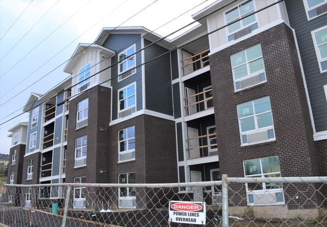 A large apartment building under construction is behind a chain link fence.