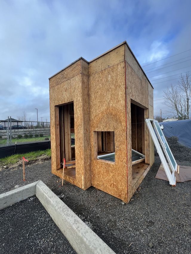 A small wooden house is being built in a dirt field.