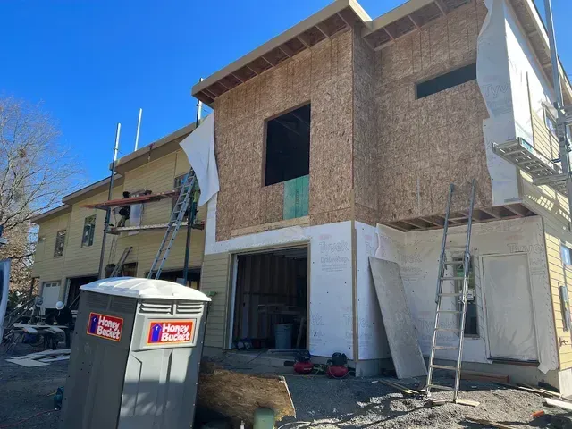 A house under construction with a portable toilet in front of it.