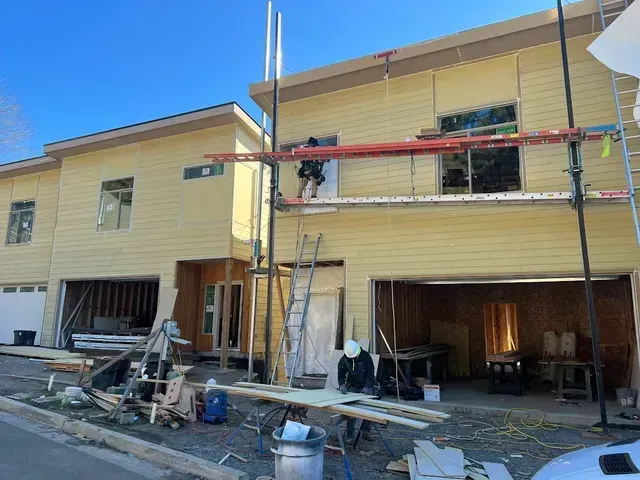 A house is being built with scaffolding and a car parked in front of it.