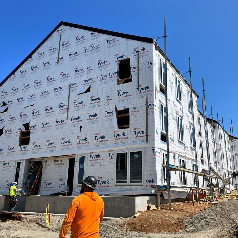 A man wearing a hard hat stands in front of a building that is under construction