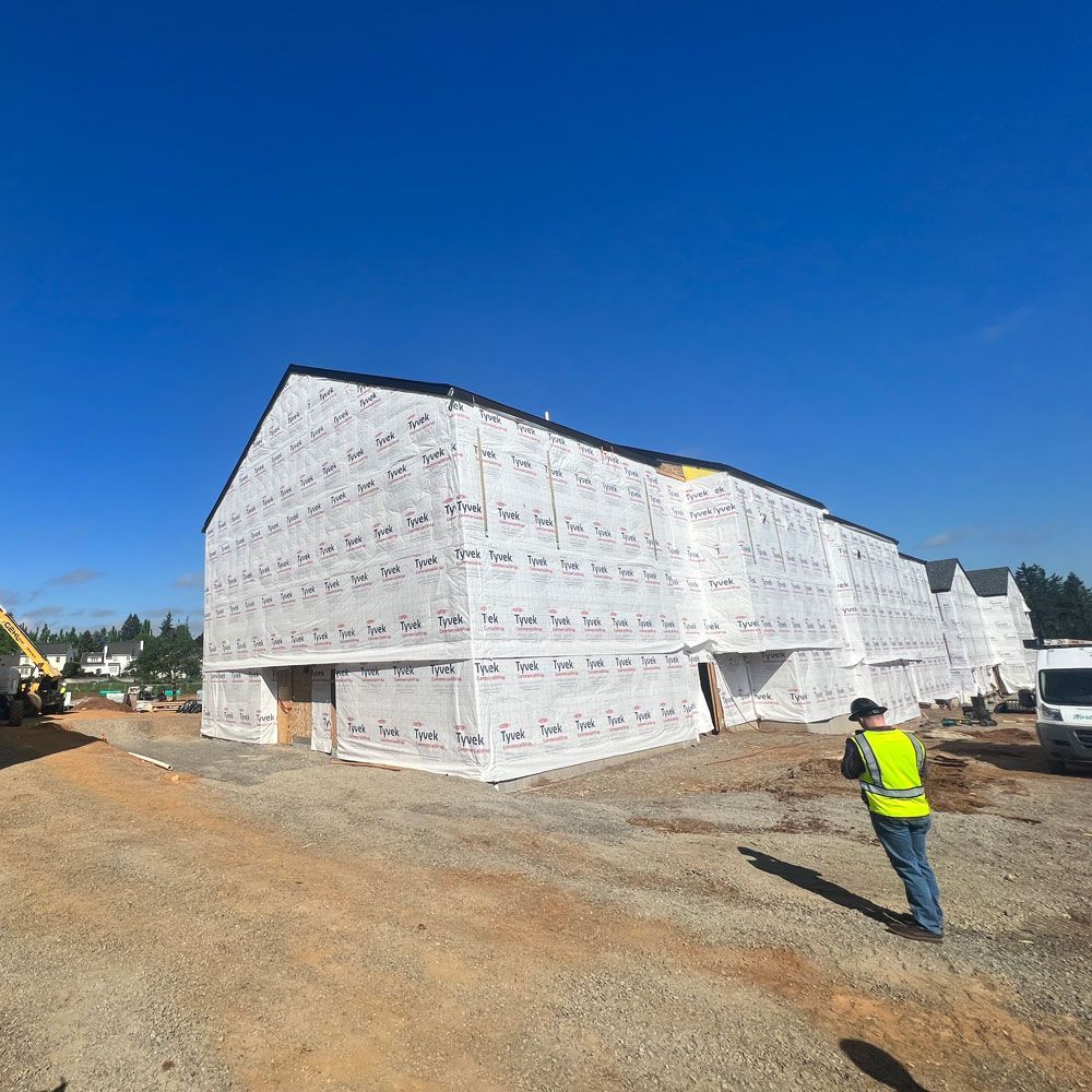A man in a yellow vest is standing in front of a building under construction.