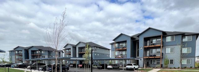 A row of apartment buildings with cars parked in front of them on a cloudy day.