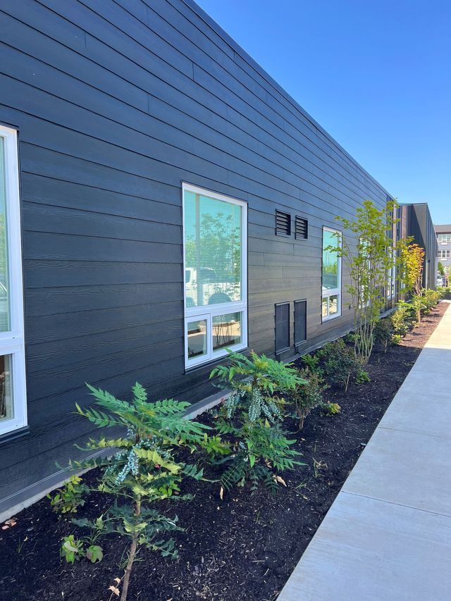A black building with white windows and a sidewalk in front of it.