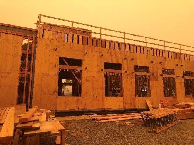 A large wooden building is being built in the middle of a field.