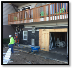 A blue wheelbarrow is in front of a house under construction
