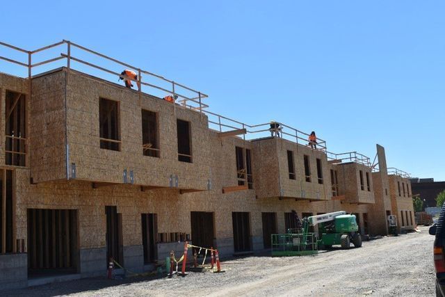 A row of buildings under construction with workers on the roofs