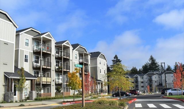 A row of apartment buildings with cars parked in front of them on a sunny day.