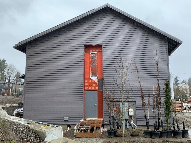 A gray house with a red door and a lot of potted plants in front of it.
