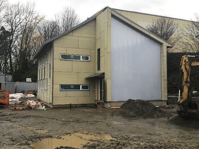 A yellow excavator is parked in front of a house under construction