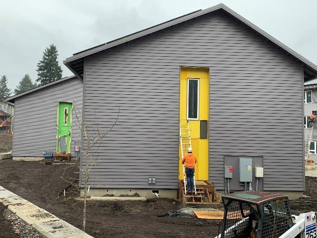 A man is standing in front of a house with a yellow door.