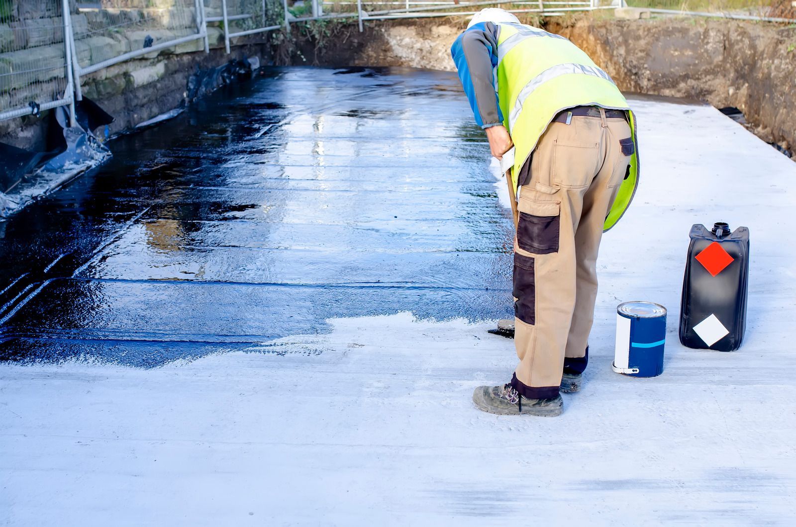 A man is painting a concrete surface with black paint.