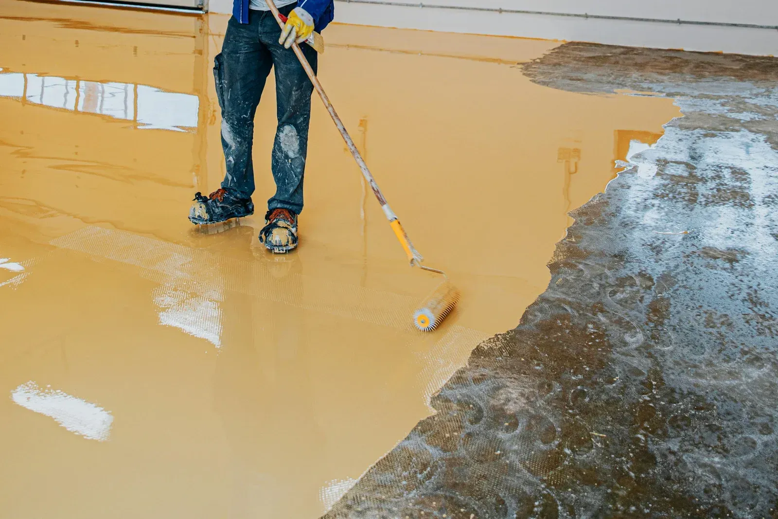 A man is painting a concrete floor with a roller.
