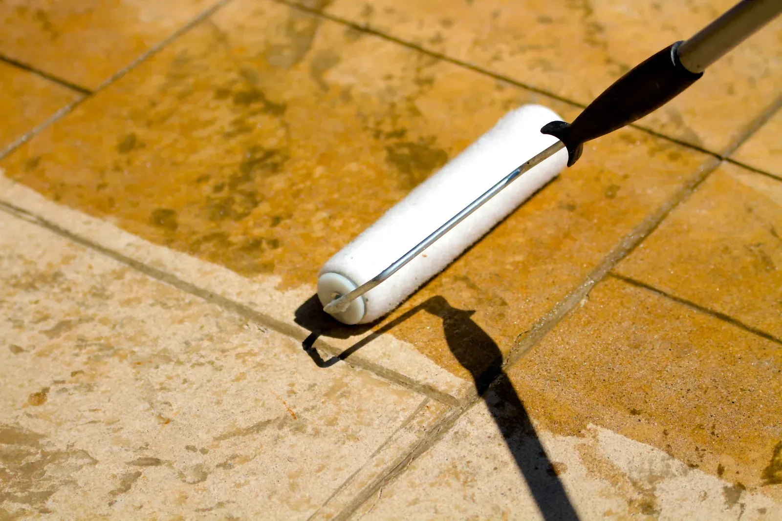A person is painting a tile floor with a roller