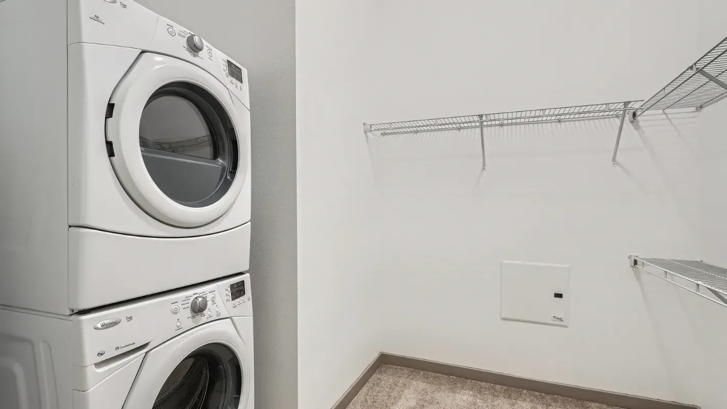 Stacked washer and dryer in a compact laundry closet with metal wire shelves.