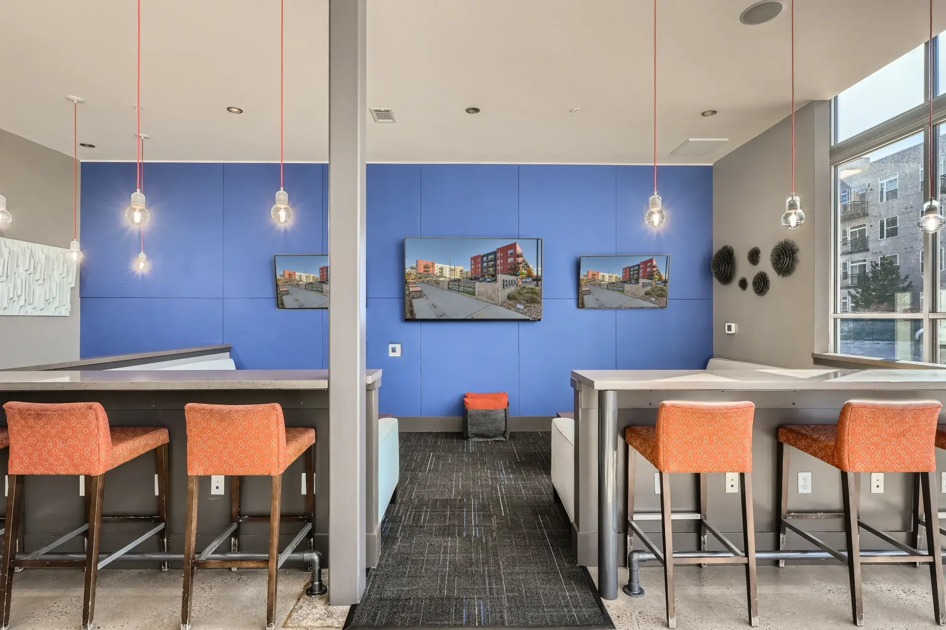 Contemporary community lounge with blue paneled wall, pendant lights, and bar-height seating.