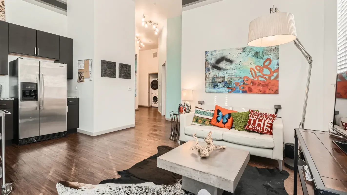 Open-concept living area with white sofa, wood floors, and stainless steel kitchen appliances.