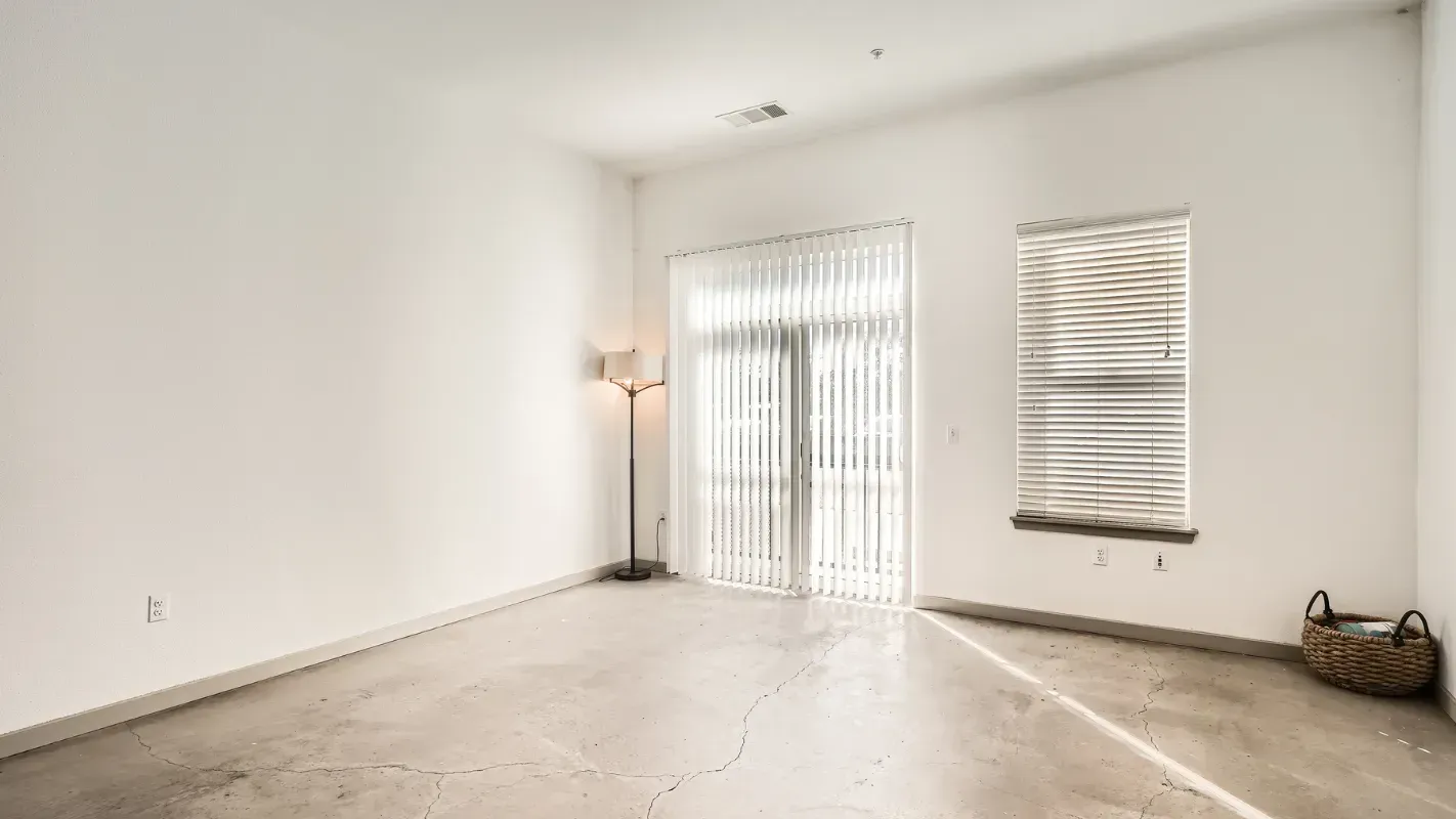 Empty living room with white walls, concrete floor, a floor lamp, and sliding glass door.