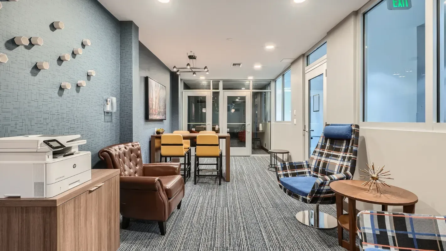 Indoor community lounge with a blue textured wall, leather chair, plaid armchairs, and a round coffee table.