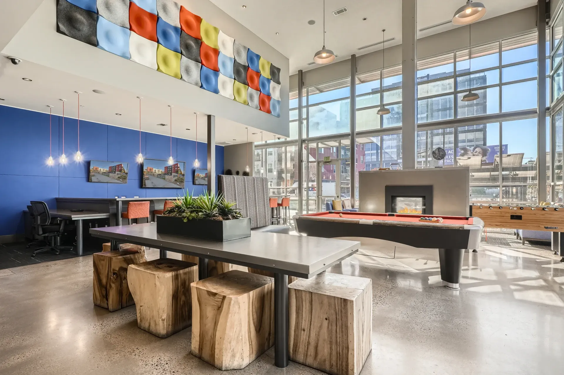 Bright, modern community lounge with a pool table, long table, colorful wall art, and large windows.