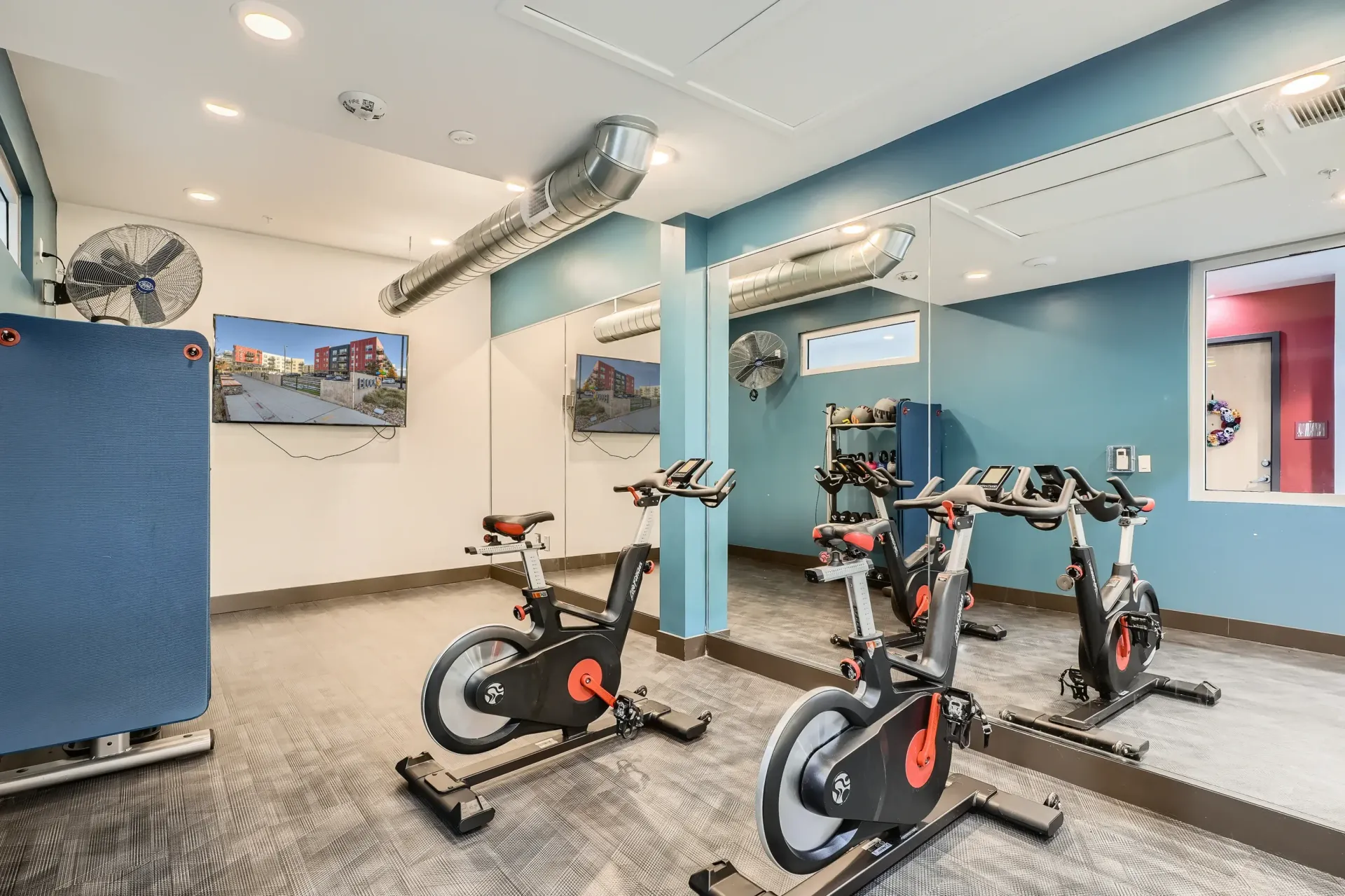 Indoor community gym with spinning bikes, mirrors, and a wall-mounted TV.