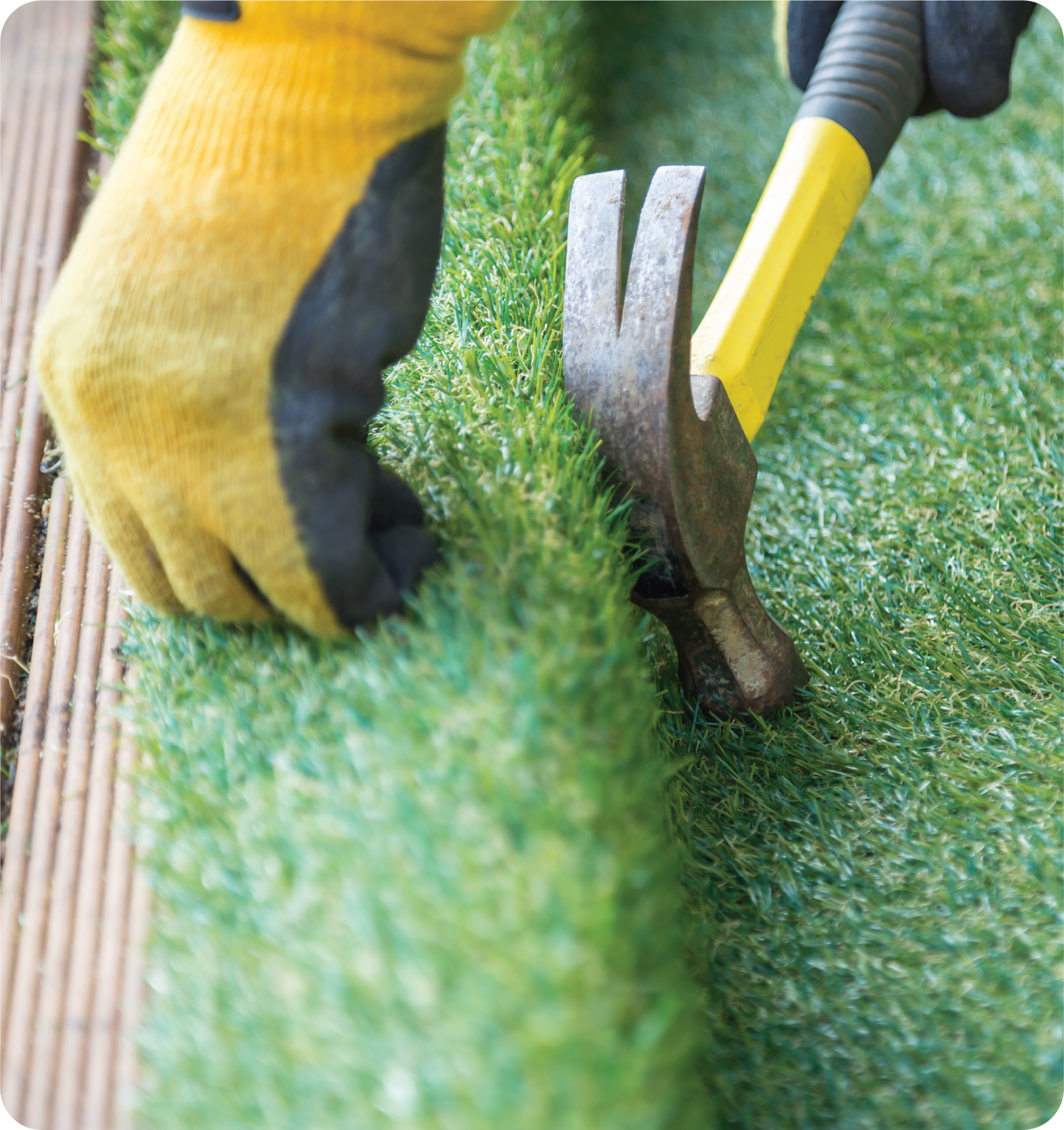 A person is using a hammer to hammer a piece of artificial grass.