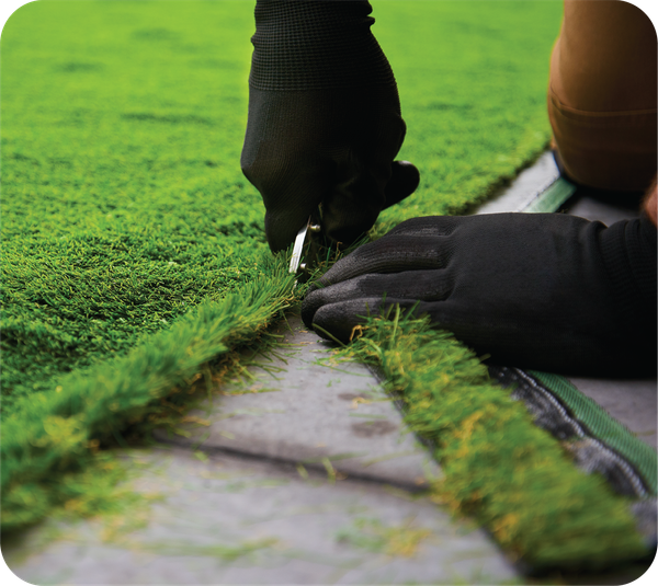 A person is cutting a piece of artificial grass with a pair of scissors.