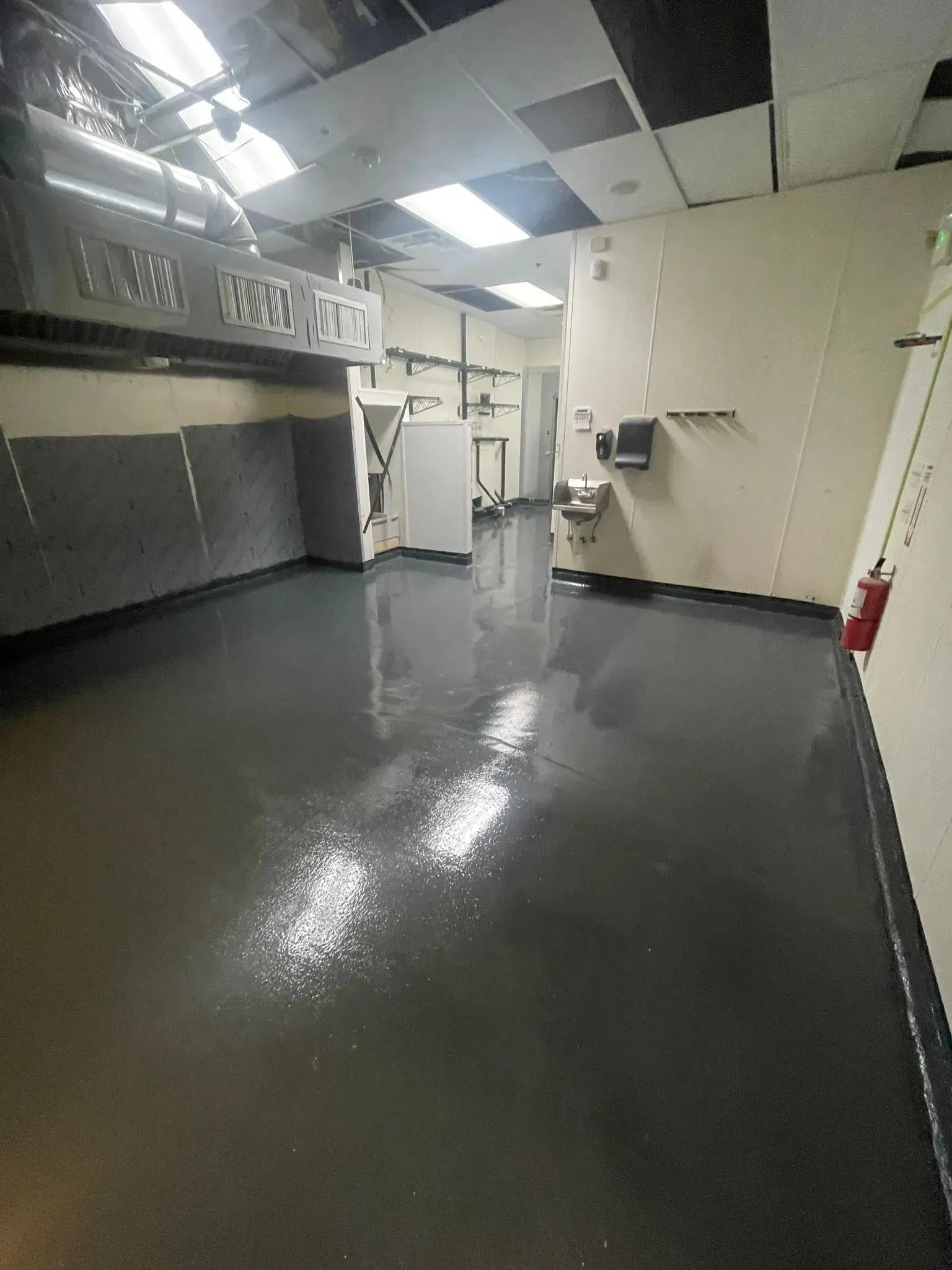 Empty industrial space with glossy gray floor, white walls, and overhead ventilation.