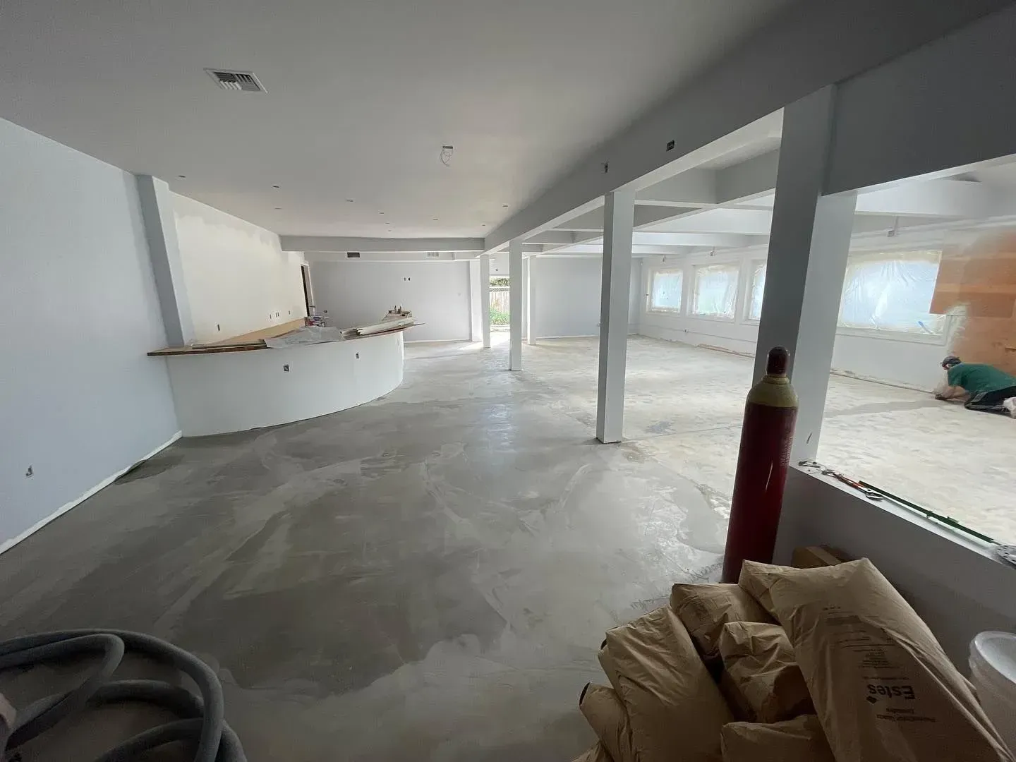 Interior of a building under construction, showing concrete floor, support pillars, and construction materials.