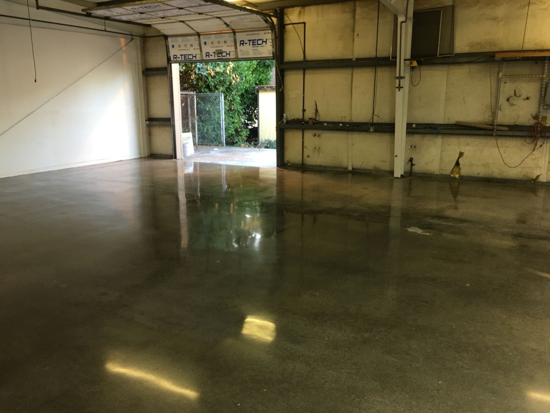 Empty industrial warehouse with polished concrete floor; open doors leading to outdoors.