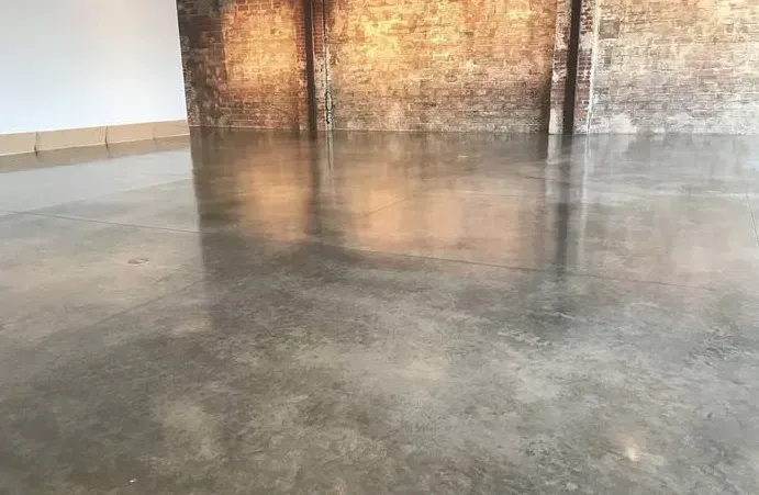 Polished gray concrete floor reflects light in an empty room with a brick wall.
