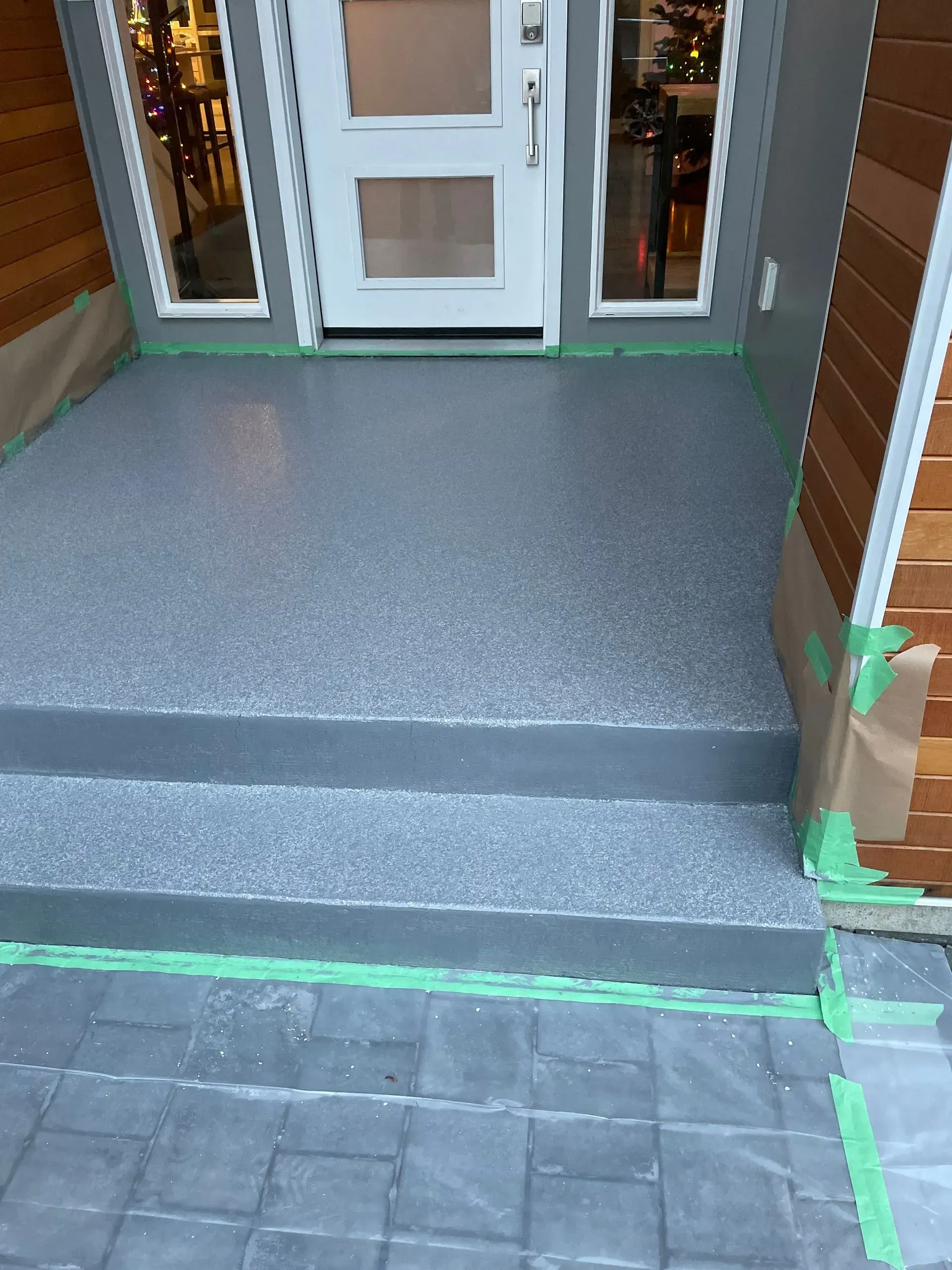 Gray epoxy-coated concrete steps leading to a white door. Green tape protects edges.