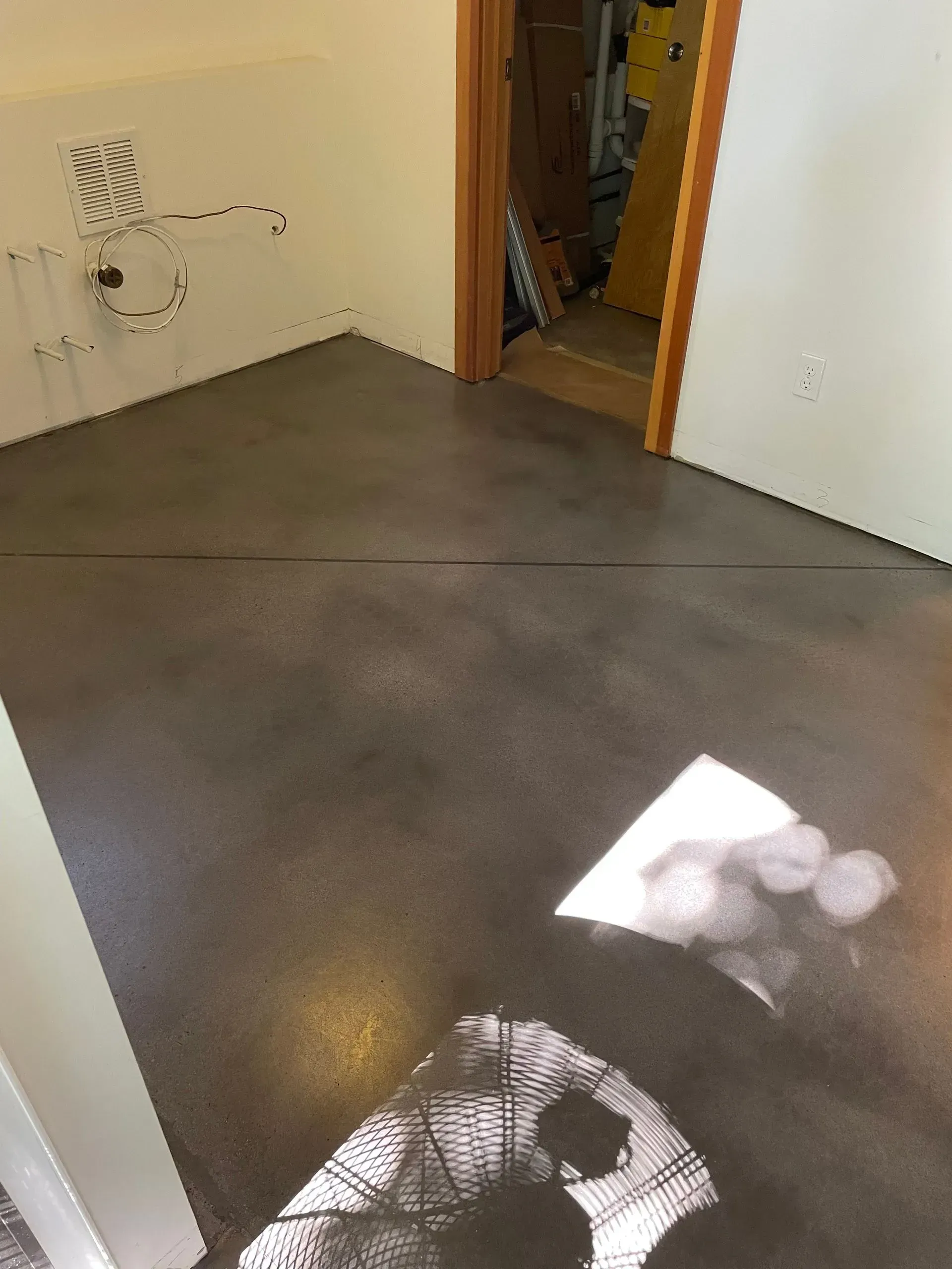 Gray stained concrete floor in a room with a doorway and white walls. Sunlight creates shadows.